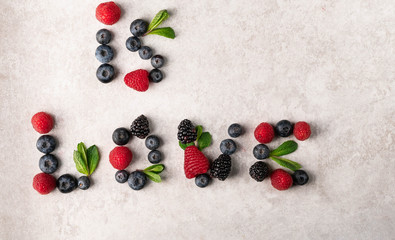 is love sign made of fresh berries and mint leaves on a light grey marble backdrop