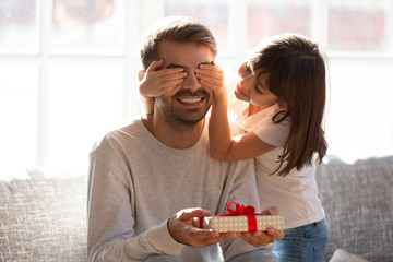 Kid daughter covering eyes of happy dad holding gift box