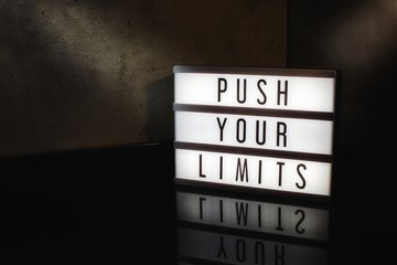 Fototapeta Push your limits motivational message on a light box in a cinematic moody background obraz
