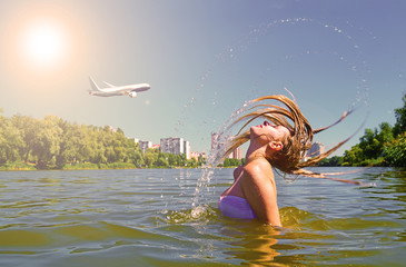 Wet girl with hair in the lake and plane in the sky blue over the city.