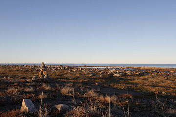 Inukshuk or Inuksuk on a rocky tundra with water in the background in late June in the arctic community of Arviat, Nunavut, Canada