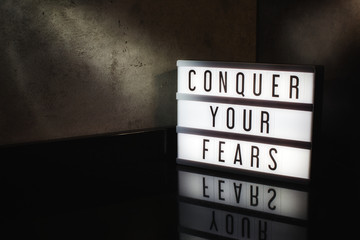 Conquer your fears motivational message on a light box in a cinematic moody background