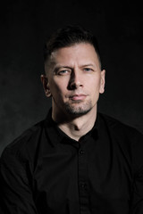 Obraz premium Portrait of a handsome man 40 years old on a dark artistic background close-up. Brunette, with gray hair, black beard and black shirt.