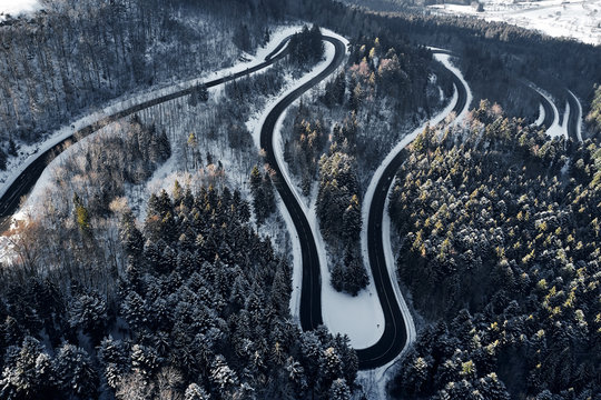 curved road in winter mountain landscape. Aerial view of forest and trees with a winding street surrounded by snow.