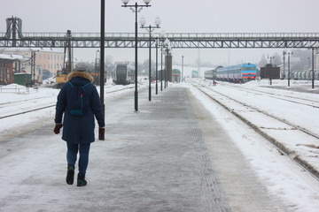 Obraz premium person walking on empty railway platform, frozen platform in the bitter cold in the winter. asphalt in the ice, waiting for the arrival of the train. meet tourists or travelers.