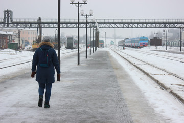 person walking on empty railway platform, frozen platform in the bitter cold in the winter. asphalt in the ice, waiting for the arrival of the train. meet tourists or travelers.