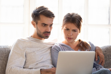 Confused baffled wife and shocked frustrated husband reading online news