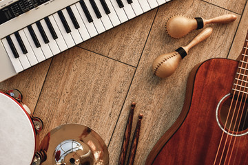 Creating a melody...Top view of musical instruments set: synthesizer, electronic guitar, wooden drum sticks, golden cymbal, drums, gold maracas and tambourine lying on wooden background. - obrazy, fototapety, plakaty