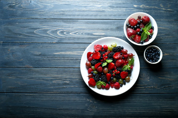 Berries in bowls on wooden background  with space for text. Composition of raspberry, currant, strawberry, blueberries, gooseberries, blackberries and mint. Health, Diet, Gardening. Harvest Concept