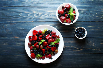 Berries in bowls on wooden background. Composition of raspberry, currant, strawberry, blueberries, gooseberries, blackberries and mint. Health, Diet, Gardening. Harvest Concept