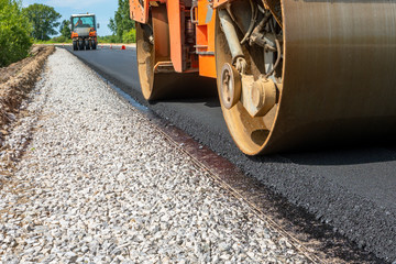 roller compacts asphalt on the road during the construction of the road. compaction of the pavement in road construction. rink goes on fresh asphalt. roller wheel closeup. hard work.