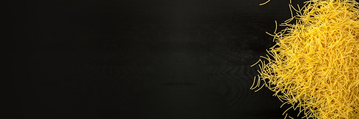 farfalle Raw vermicelli italian pasta on a wood black textured background. Close-up view from the top. Free space for text. BAnner