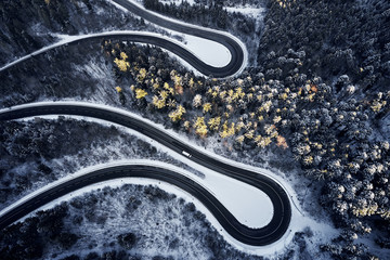 Aerial drone view of a curved winding road through the forest high up in the mountains in the winter with snow covered trees and curved streets in winter