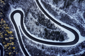 Aerial drone view of a curved winding road through the forest high up in the mountains in the winter with snow covered trees and curved streets in winter