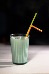 A glass of milk in a transparent faceted glass cupwith straw on a black background