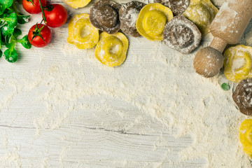 Homemade fresh Italian ravioli pasta on white wood table  with flour, basil, tomatoes,background,top view.