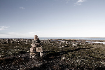 Inukshuk or Inuksuk on a rocky tundra with water in the background in late June in the arctic community of Arviat, Nunavut, Canada - refined