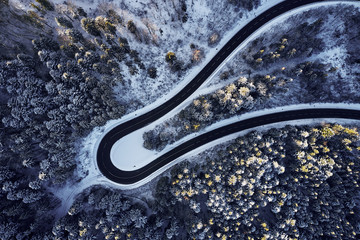 Aerial drone view of a curved winding road through the forest high up in the mountains in the winter with snow covered trees and curved streets in winter