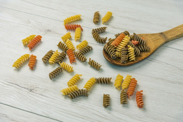 Naklejka premium Raw uncooked three-colored Fusilli on white wood table.