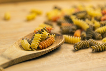 Raw uncooked three-colored Fusilli in a spoon on wood table.
