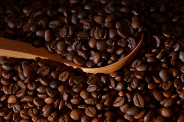 A pile of roasted coffee beans with a wooden ladle