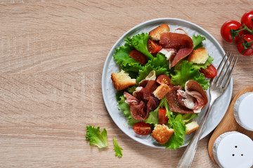 Salad with prosciutto, cherry tomatoes, bread crisps on the kitchen table. View from above.
