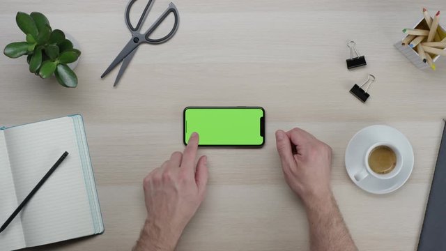 Male hands using smart device with green screen chroma on wooden clean minimalistic table with top view