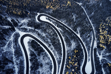 Aerial drone view of a curved winding road through the forest high up in the mountains in the winter with snow covered trees and curved streets in winter