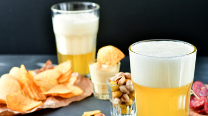 two glasses of beer and snacks chips, nachos with sauce, pistachios and salami, aperitif, relax in the bar with friends, beer party.  selective focus and copy space