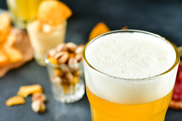 two glasses of beer and snacks chips, nachos with sauce, pistachios and salami, aperitif, relax in the bar with friends, beer party.  selective focus and copy space