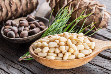 Pine nuts in the spoon and pine nut cone on the wooden table. Organic food.