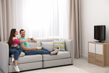 Obraz premium Couple with snack watching TV on sofa together at home. Space for text