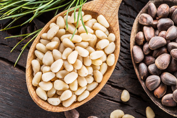 Pine nuts in the spoon and pine nut cone on the wooden table. Organic food.