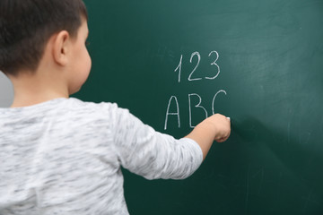 Little child writing letters and numbers on chalkboard