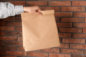 Woman holding paper bag against brick wall. Mockup for design