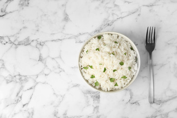 Bowl of boiled rice and fork on marble background, top view with space for text