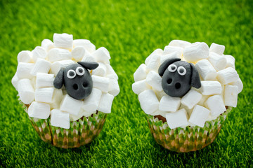 Easter sheep cupcakes on green grass background, homemade cup cakes shaped funny sheeps with...