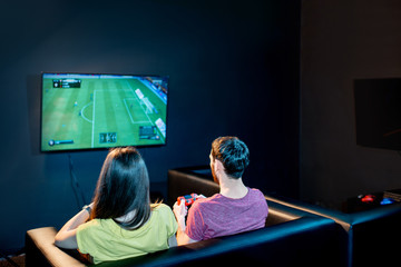 Young couple playing football game with gaming console sitting on the couch at the playing club,...