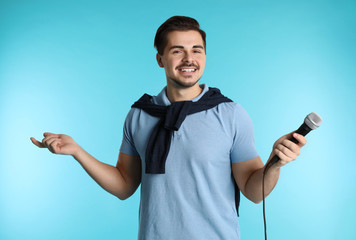 Young handsome man in casual clothes posing with microphone on color background