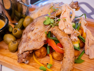 Close up shot of a plate with duck leg, sausage, bread