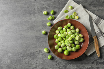 Plate of fresh Brussels sprouts, napkin and knife on grey background, top view with space for text