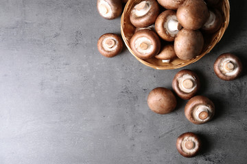 Obraz premium Wicker bowl and fresh champignon mushrooms on grey background, top view with space for text