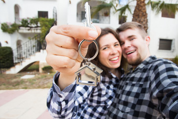 Property, real estate and rent concept - Happy funny young couple showing a keys of their new house