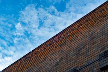 Fototapeta na wymiar Background from the wall of a brick building and a blue sky with clouds divided diagonally