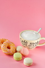 large Cup of cappuccino coffee and donuts and a lot of colorful  French macarons, on the Cup inscription in French (mocha coffee, coffee with milk). pink background, selective focus,without logo