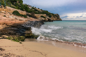 Wellen brechen sich weiß schäumend am sandig, felsigen Strand auf Mallorca