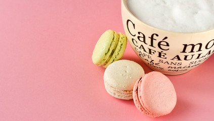 large Cup of cappuccino coffee and a lot of colorful  French macarons. pink background, selective focus. on the Cup inscription in French (mocha coffee, coffee with milk) without logos