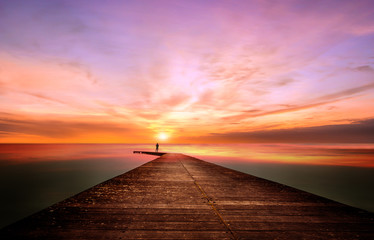 Obraz na płótnie Canvas A person on a pier observes and contemplates a splendid sunset
