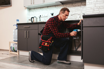 Handyman at work. Repairing kitchen shelves by perforator