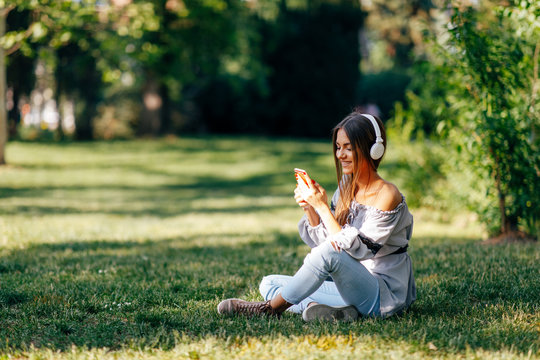 Young woman listens to music via headphones and smartphone in the park